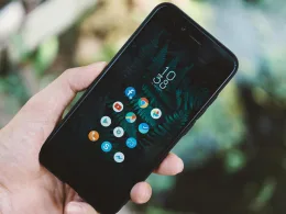 Close-up of a hand holding a smartphone with app icons and a nature wallpaper.