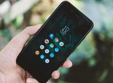 Close-up of a hand holding a smartphone with app icons and a nature wallpaper.