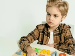 A young boy in a plaid shirt playing with colorful letters on a table indoors.