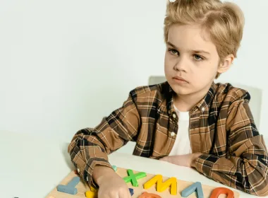 A young boy in a plaid shirt playing with colorful letters on a table indoors.