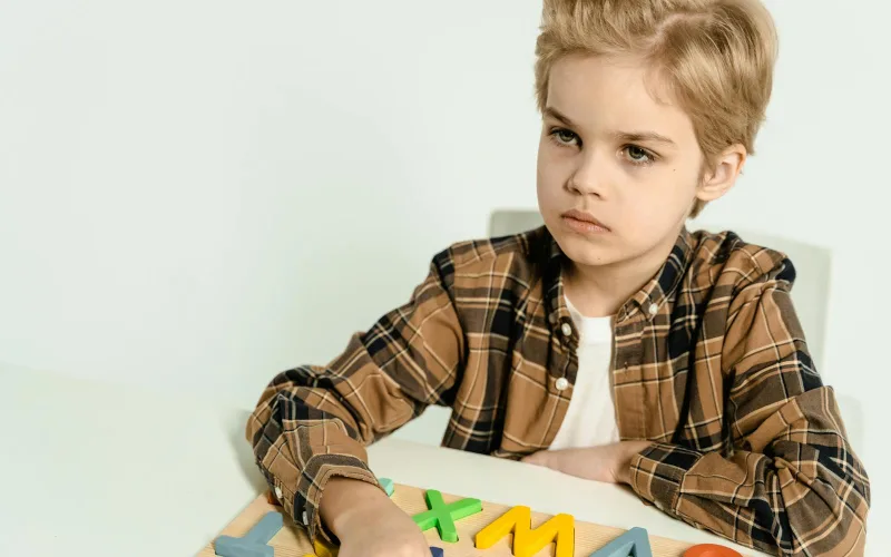A young boy in a plaid shirt playing with colorful letters on a table indoors.