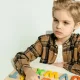 A young boy in a plaid shirt playing with colorful letters on a table indoors.