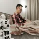 A modern bedroom featuring a robot on a bedside table and a man sitting on a bed.